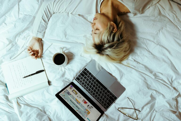 Woman lying on her bed with an open laptop and notebook beside her, eyes closed, not working