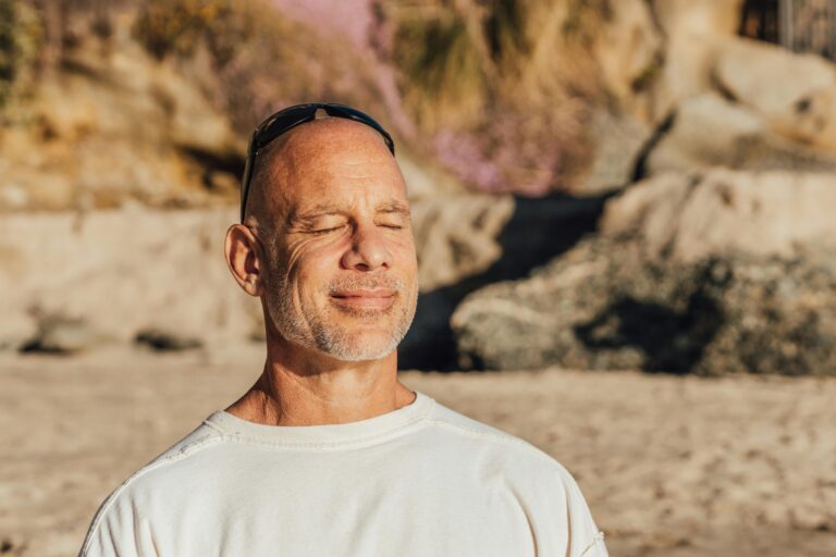 Man standing outdoors with eyes closed, face relaxed in the sunlight — illustrating a moment of deliberate breathing and vagus nerve activation.