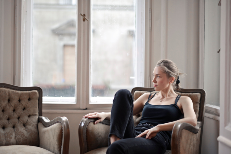 Woman sitting with a tense, guarded expression and closed posture, illustrating the fight response — the defensiveness and edge that build under the surface before any outward sign appears.