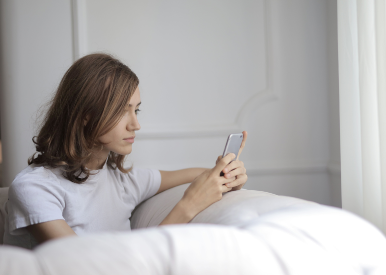 Woman reading a message on her phone with a focused expression, illustrating the moment just before the nervous system activates a fight, flight, freeze, or fawn response.
