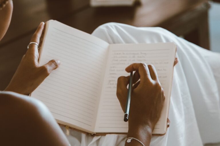 Person writing by hand in a journal, illustrating the practice of recording real evidence over time — the habit that makes a self-affirmation something the brain can actually check against memory.