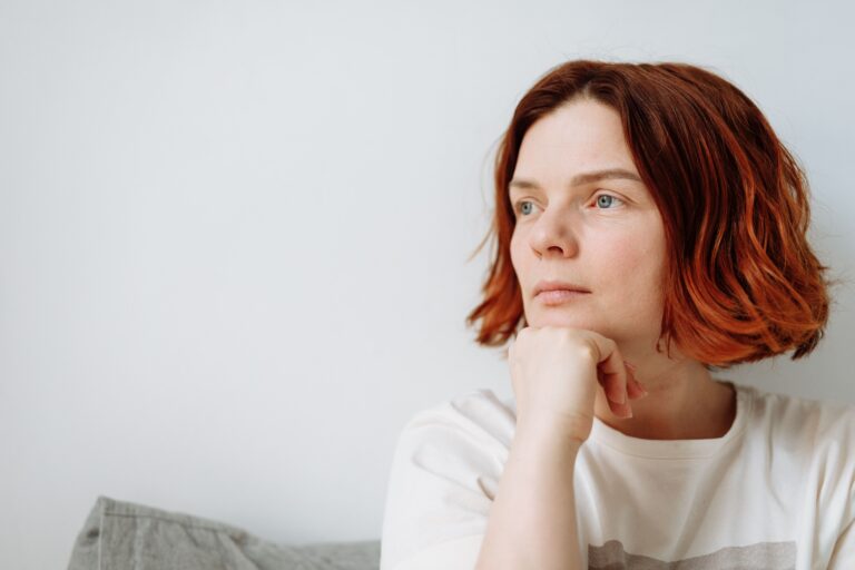 Woman resting her chin on her hand with a quiet, distant expression, illustrating the experience of always feeling anxious for no reason — the low-level hum that never fully switches off.