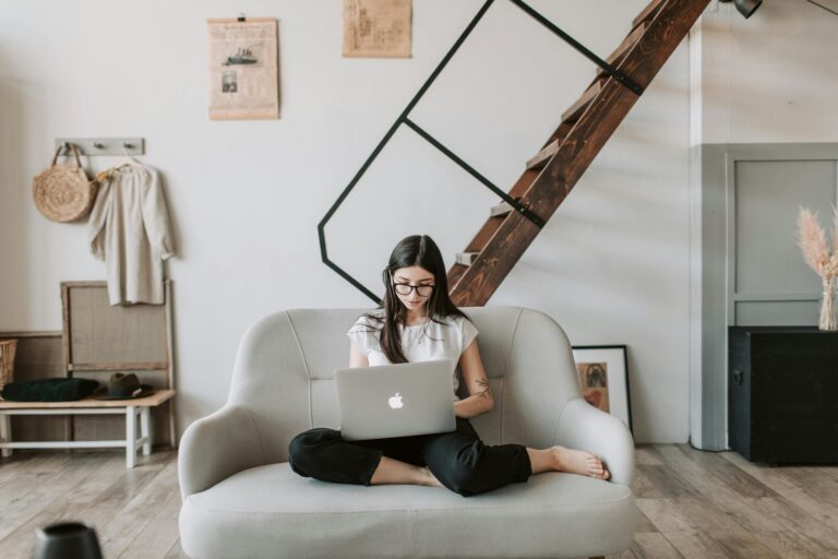 Woman sitting cross-legged on a sofa working on a laptop, illustrating the practice of working with the avoidance pattern one small step at a time.