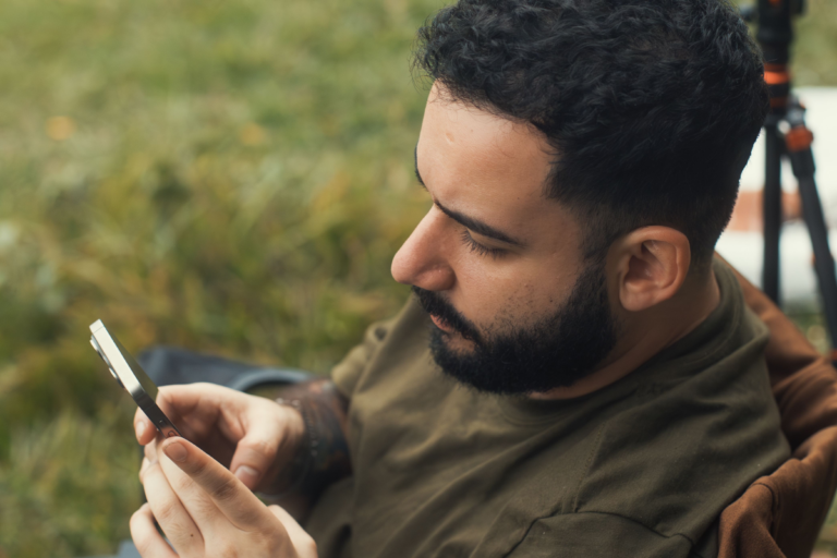 Man sitting outdoors looking at his phone with a tense, unfocused expression, illustrating the hidden signs of anxiety that show up in ordinary moments — present but not quite there
