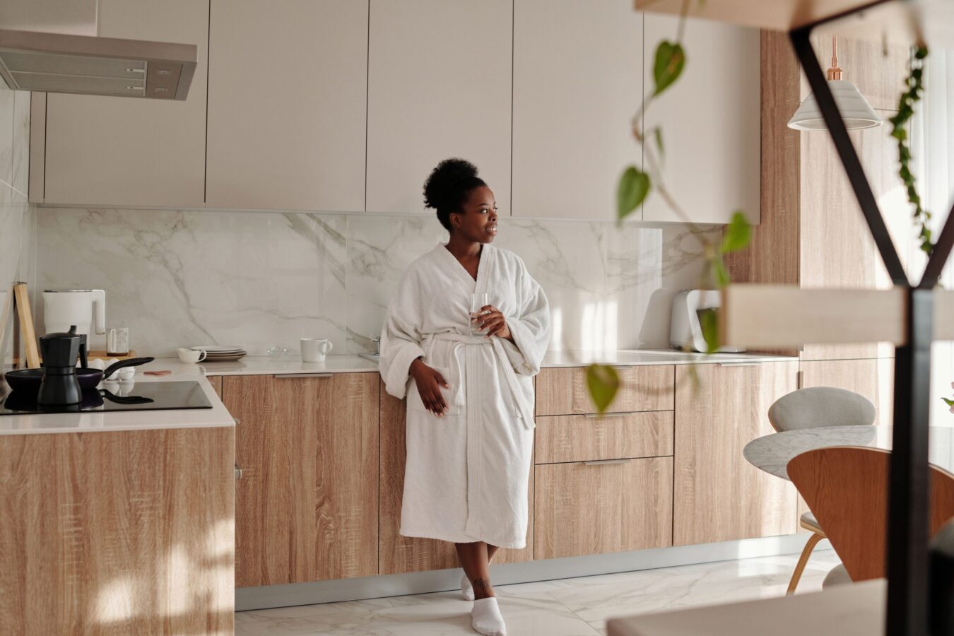 Woman in a bathrobe standing quietly in her kitchen in the morning, illustrating the practice of being ordinary without needing to perform or produce anything.